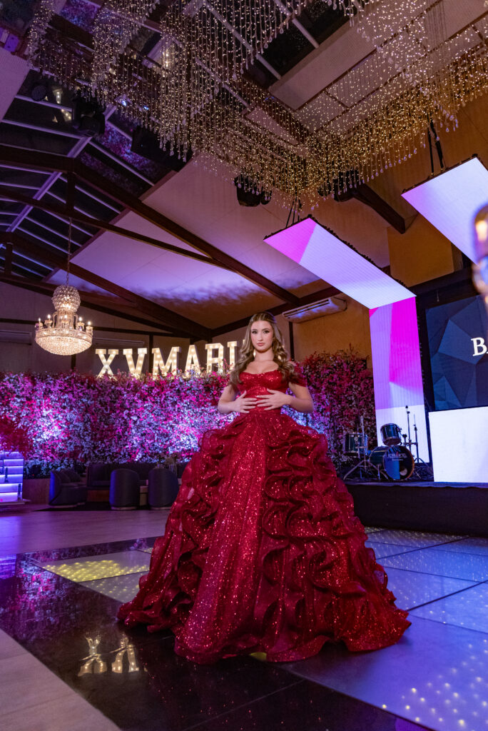 Debutante em vestido vermelho na pista iluminada diante do letreiro luminoso