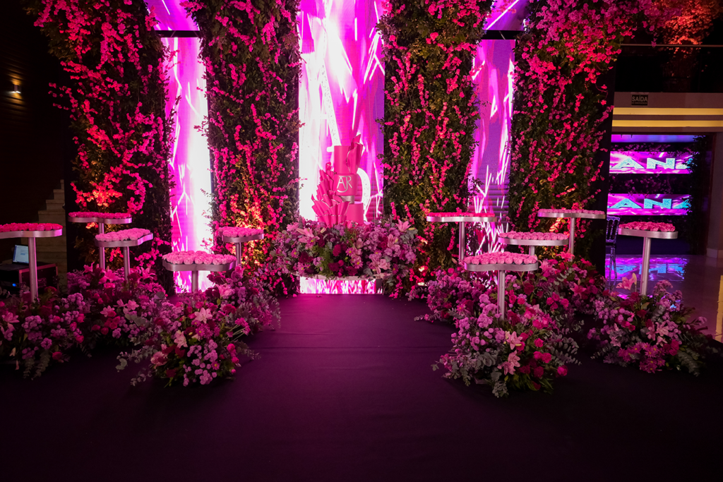 Corredor decorado com flores em tons de rosa e iluminação neon na entrada da festa