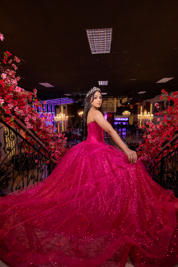 Debutante em vestido pink entre arranjos de flores em tons de rosa e vermelho