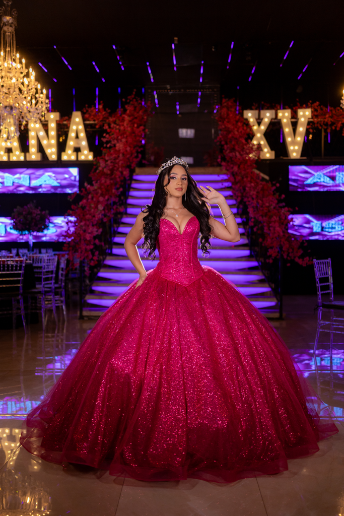 Debutante em vestido pink na escadaria decorada com flores vermelhas e painéis de LED