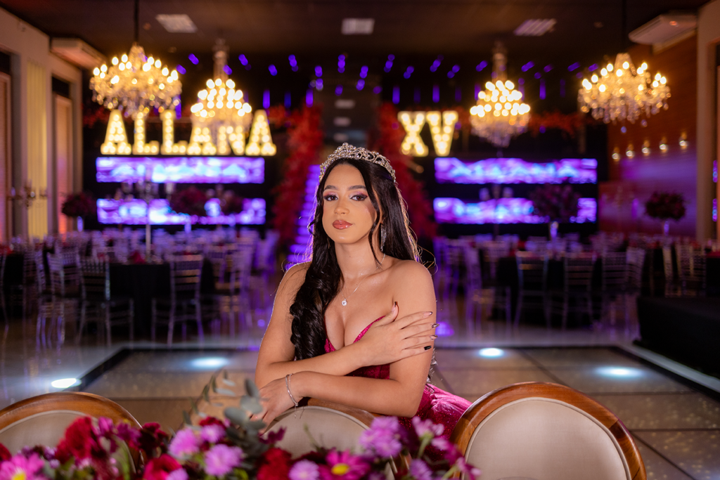Allana apoiada em poltrona dourada diante do salão decorado em pink e neon