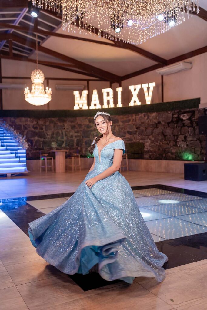 Mariana em vestido azul diante do letreiro luminoso com seu nome