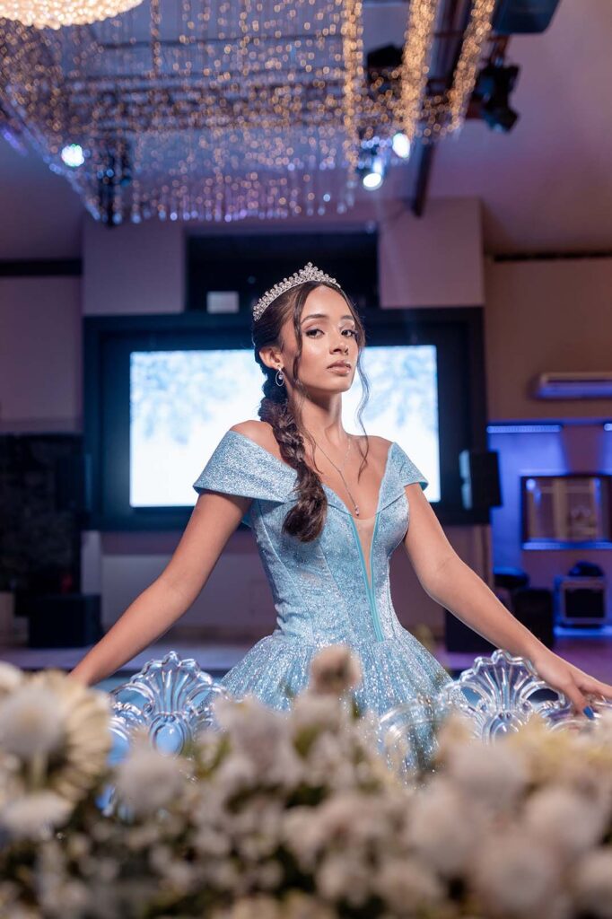 Debutante em vestido azul com os braços abertos diante do telão