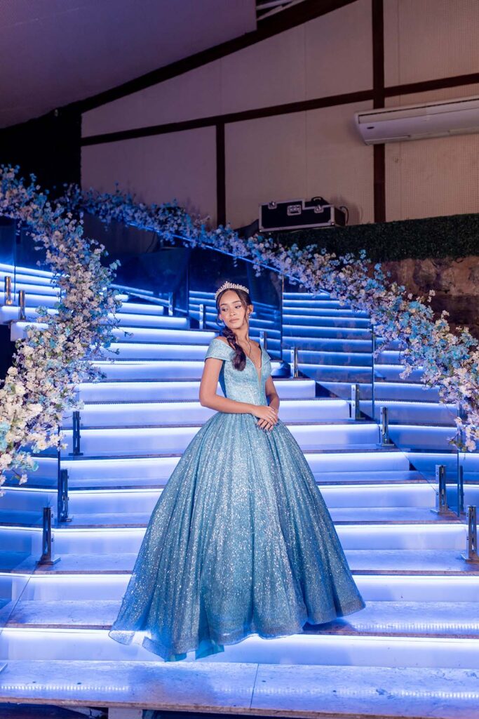 Debutante desce a escadaria iluminada em azul decorada com flores