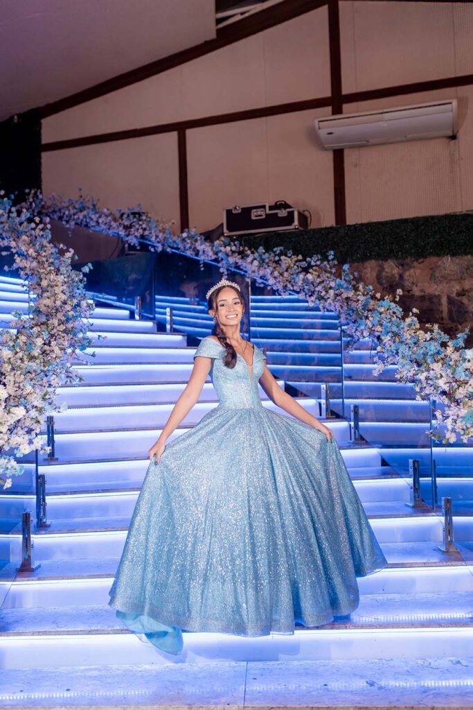 Debutante em vestido azul na escadaria iluminada da festa de 15 anos