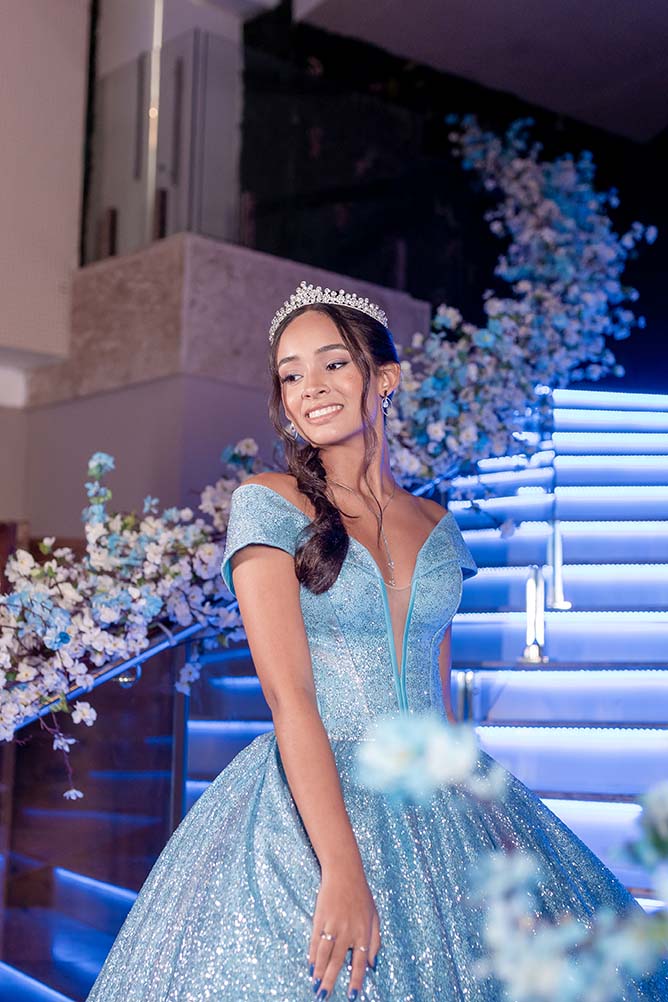 Debutante em vestido azul ao lado da escadaria iluminada