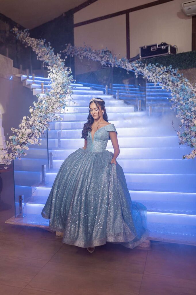 Debutante em vestido azul no centro da escadaria iluminada