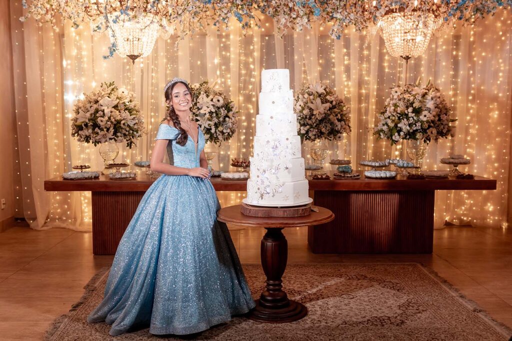 Debutante em vestido azul ao lado do bolo de 15 anos