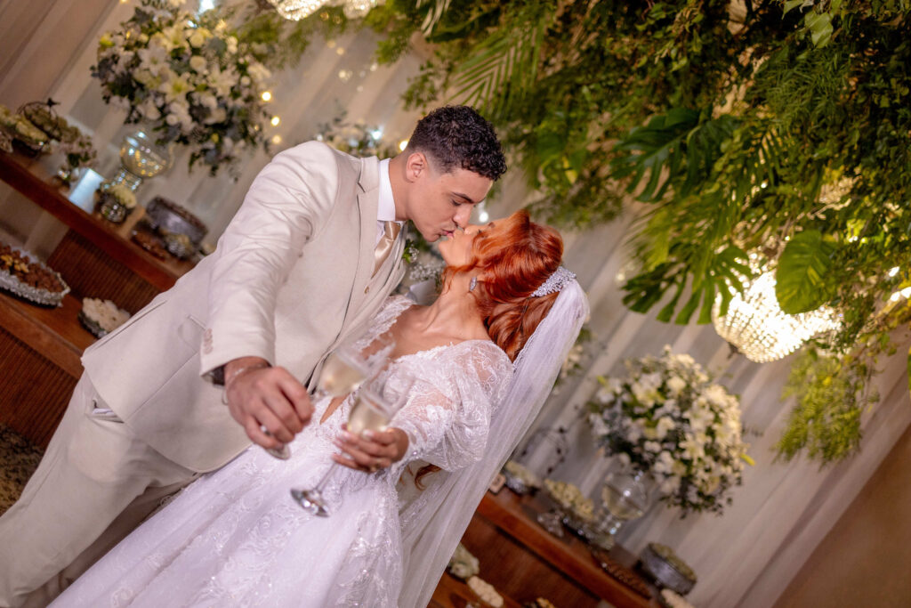 Noivo beija a noiva diante do arranjo de folhagens