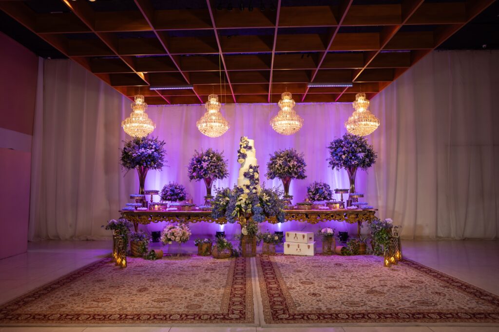 Salão da recepção de casamento com mesa do bolo, lustres e iluminação em lilás