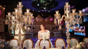 Noiva sentada à mesa dos noivos entre candelabros de cristal