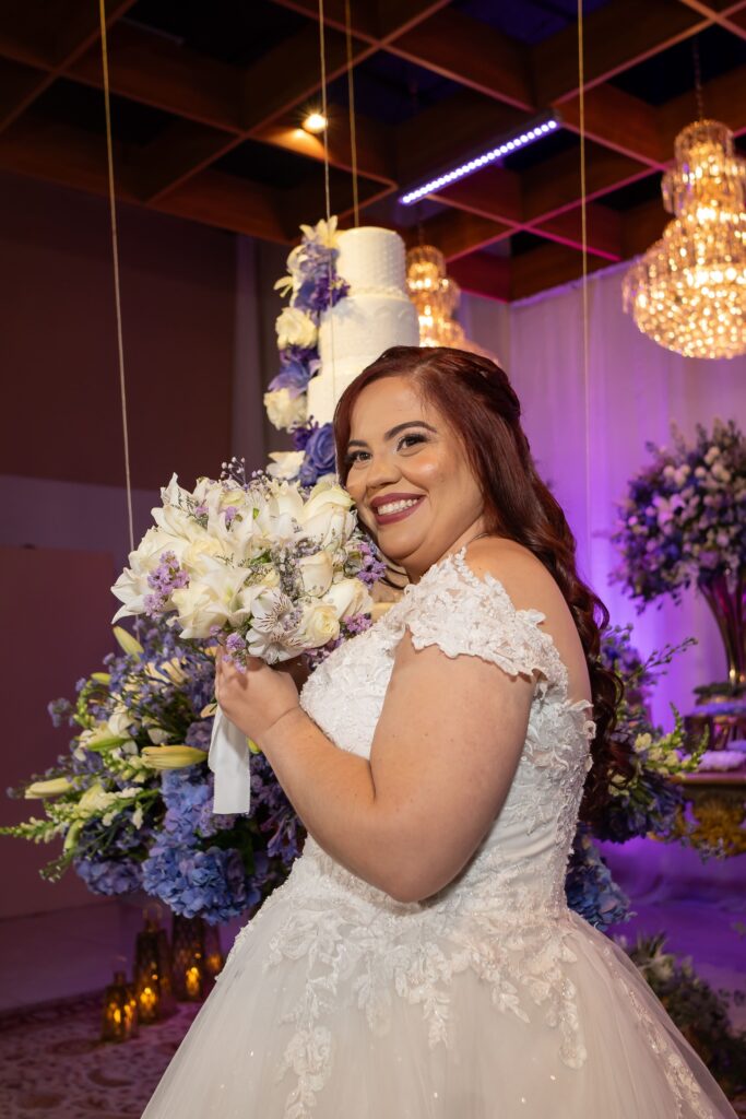 Noiva com o buquê diante do bolo de casamento decorado com flores
