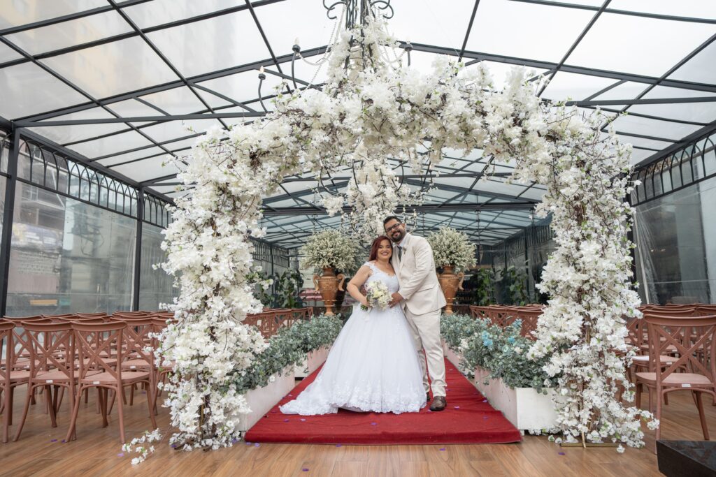 Cerimônia de casamento sob tenda de vidro com arco floral e tapete vermelho