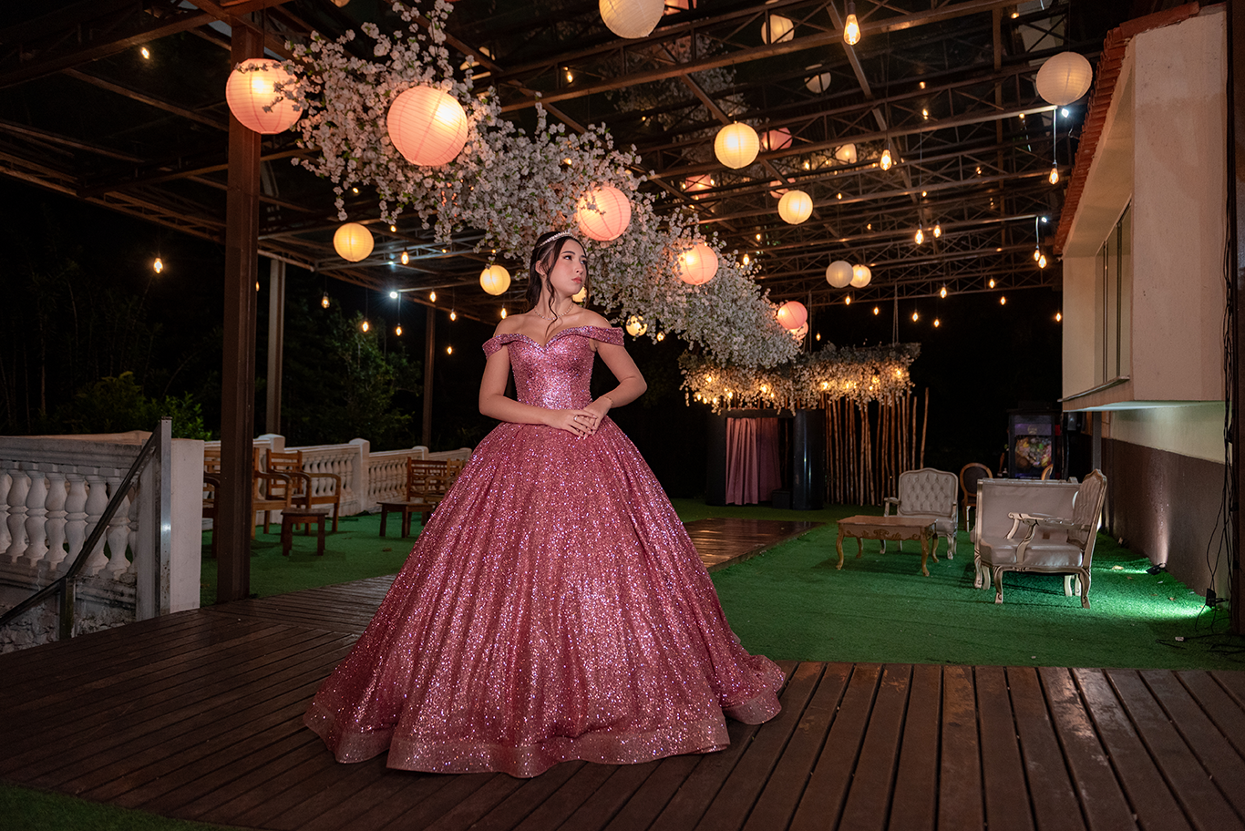 Debutante em vestido rosé na área externa decorada com lanternas e flores brancas