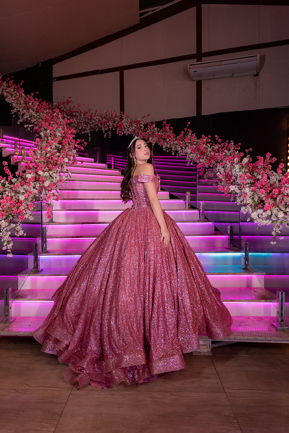 Debutante em vestido rosé na escadaria iluminada em tons de rosa
