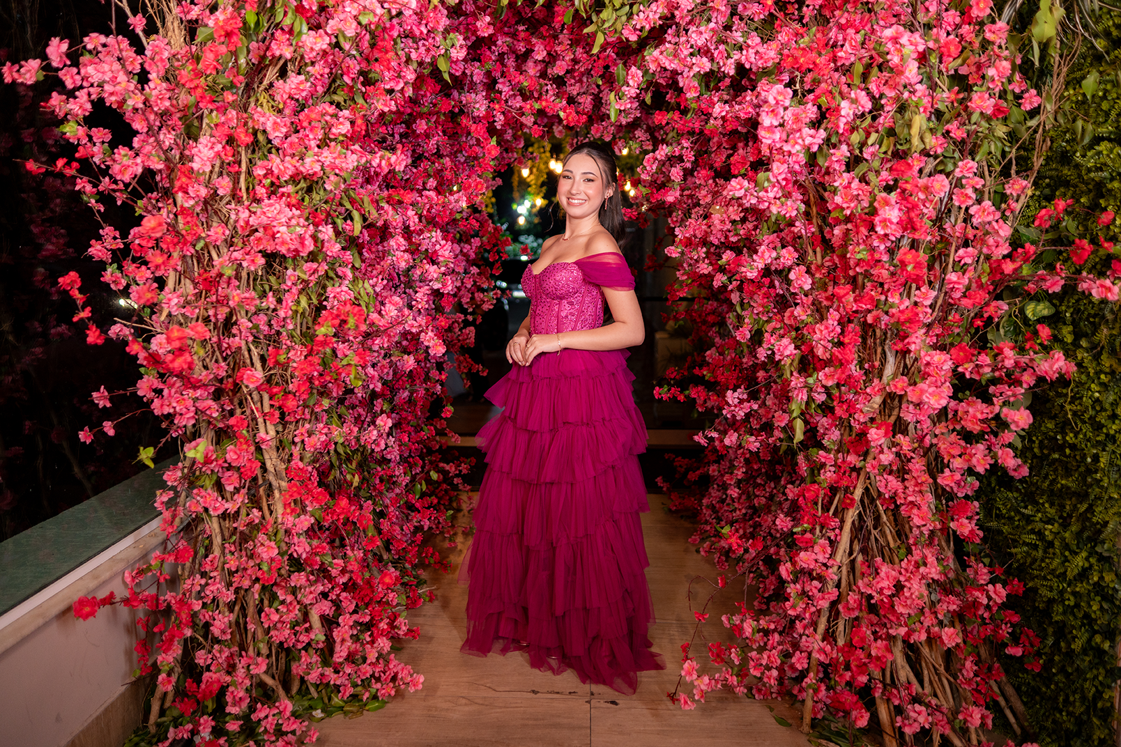Debutante em vestido pink emoldurada por um arco de flores vermelhas