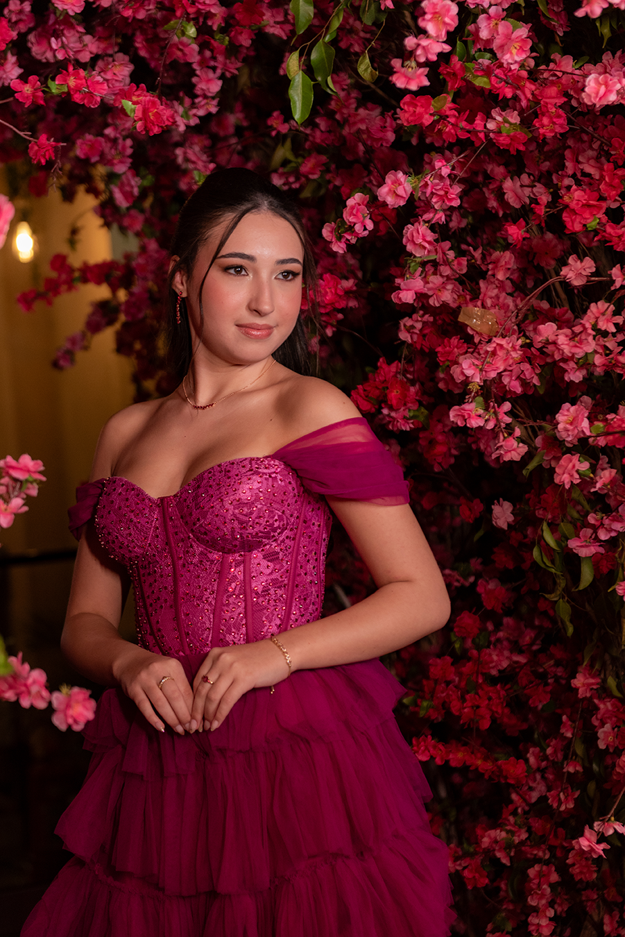 Debutante em vestido pink diante do arco de flores vermelhas e rosa