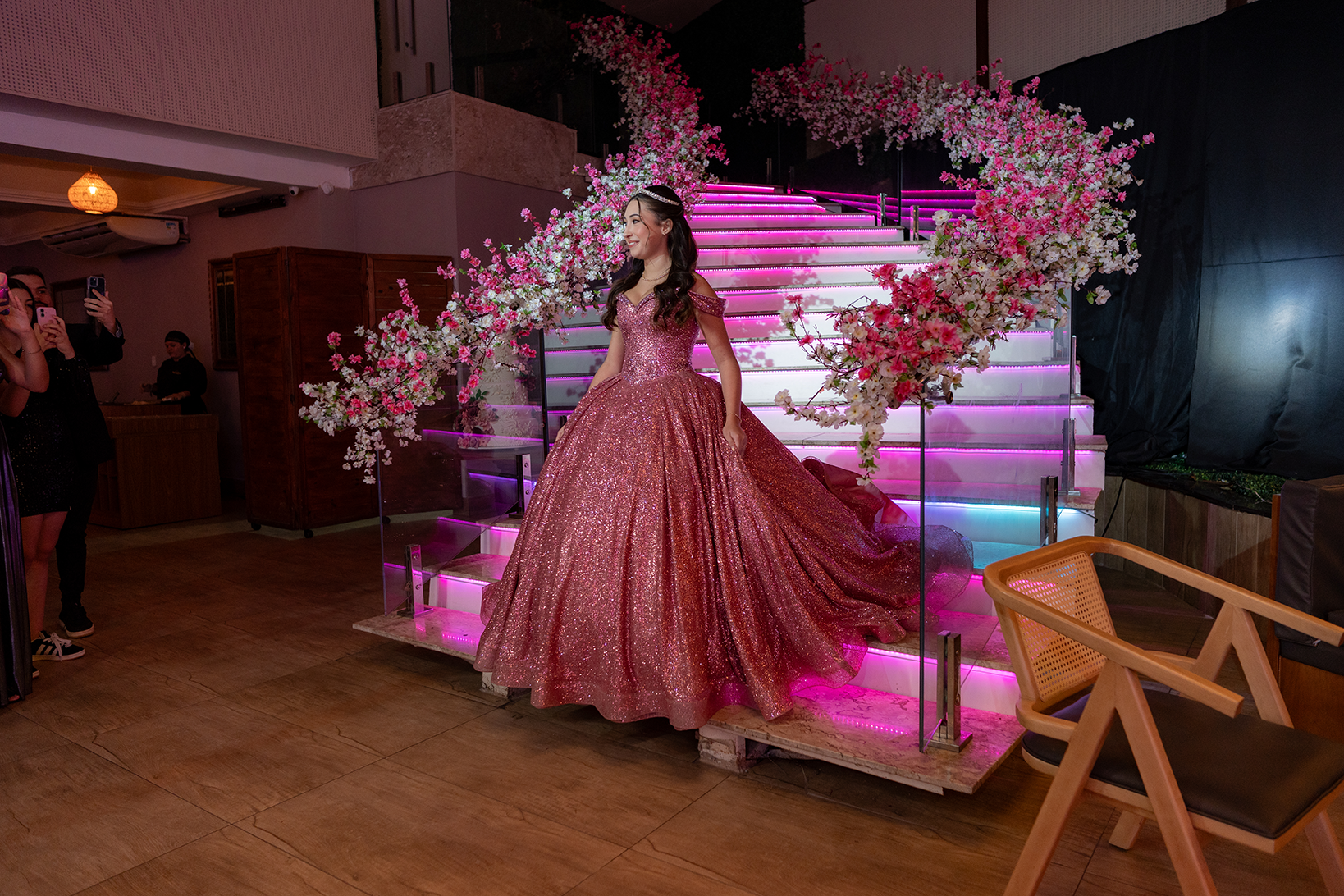 Debutante em vestido rosé ao lado da escadaria decorada com flores
