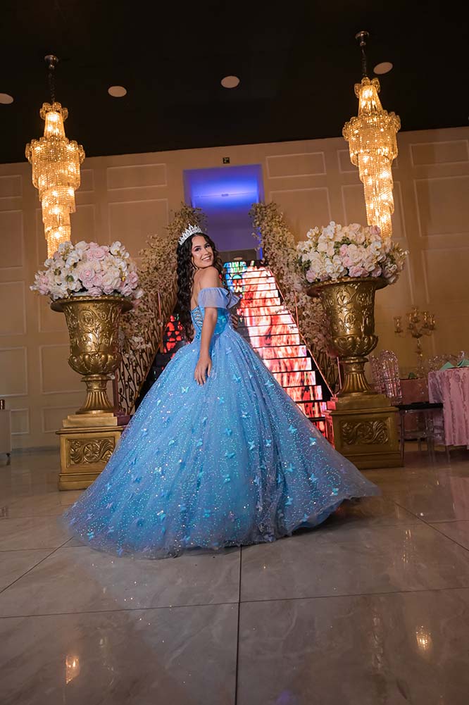 Debutante em vestido azul entre vasos dourados de flores