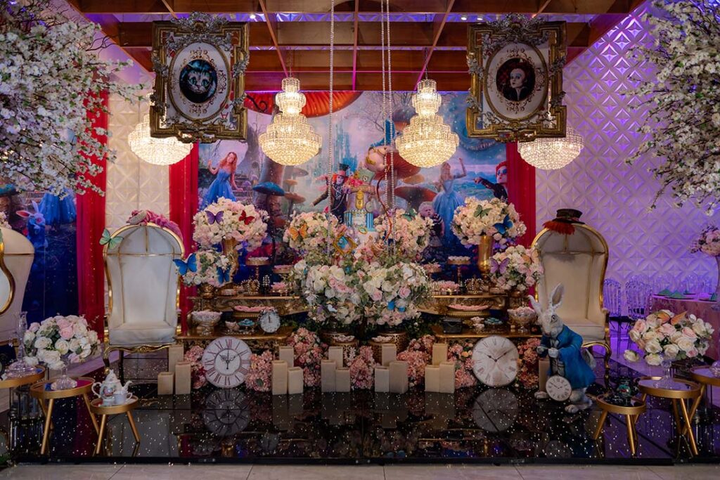 Mesa do bolo decorada com cartas, quadros e flores em tons pastel