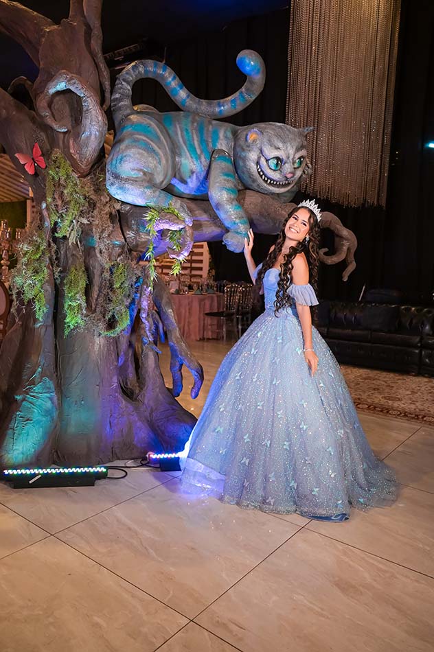 Debutante em vestido azul ao lado do Gato de Cheshire cenográfico