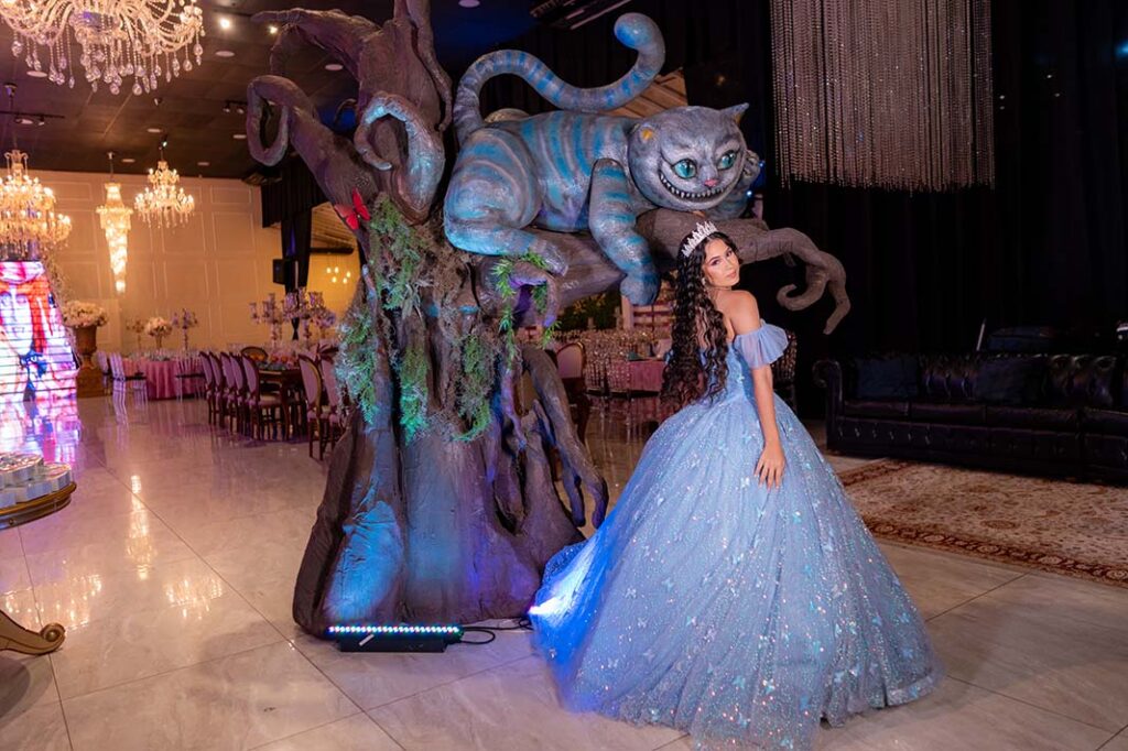 Debutante em vestido azul diante do Gato de Cheshire e da decoração