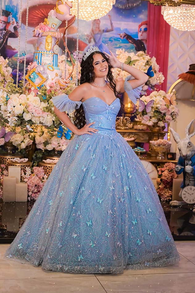 Debutante em vestido azul entre os arranjos de flores da mesa do bolo
