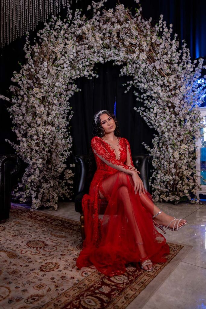 Debutante em vestido vermelho sob o arco de flores brancas
