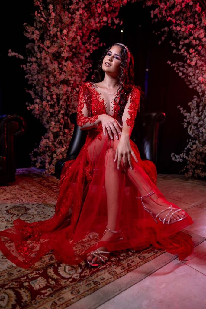 Anna Caroline no segundo look vermelho sentada diante das flores