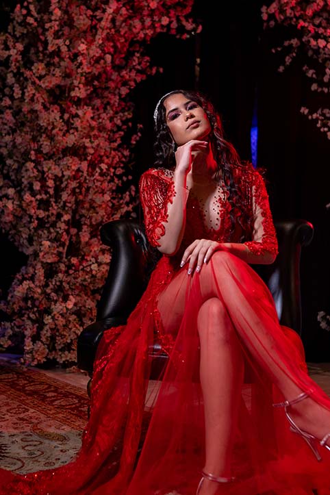 Debutante em vestido vermelho sentada diante da parede de flores