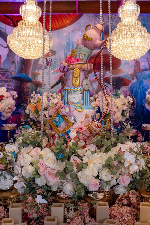 Mesa do bolo com flores, xícaras e elementos do tema Alice no País das Maravilhas