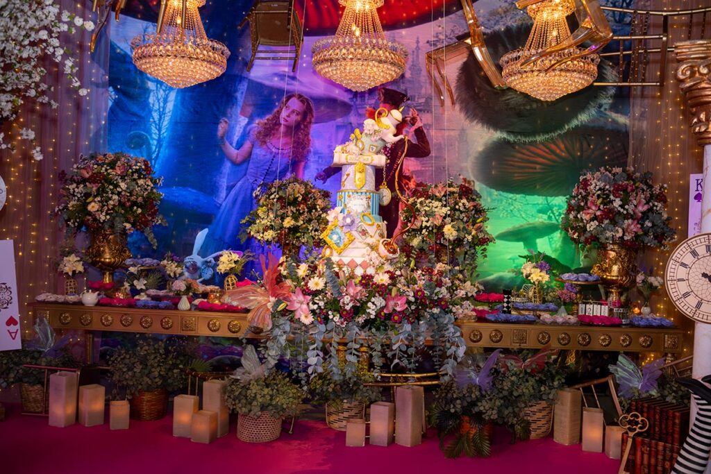 Mesa do bolo decorada com flores, relógios e elementos do tema Alice no País das Maravilhas