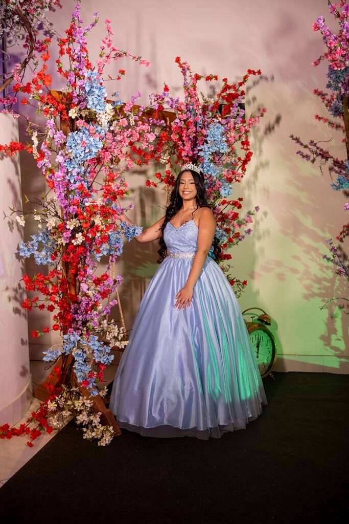 Debutante em vestido azul diante da parede de flores vermelhas