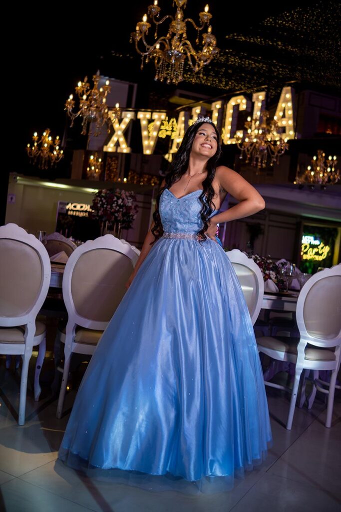 Alicia em vestido azul diante do letreiro luminoso com seu nome