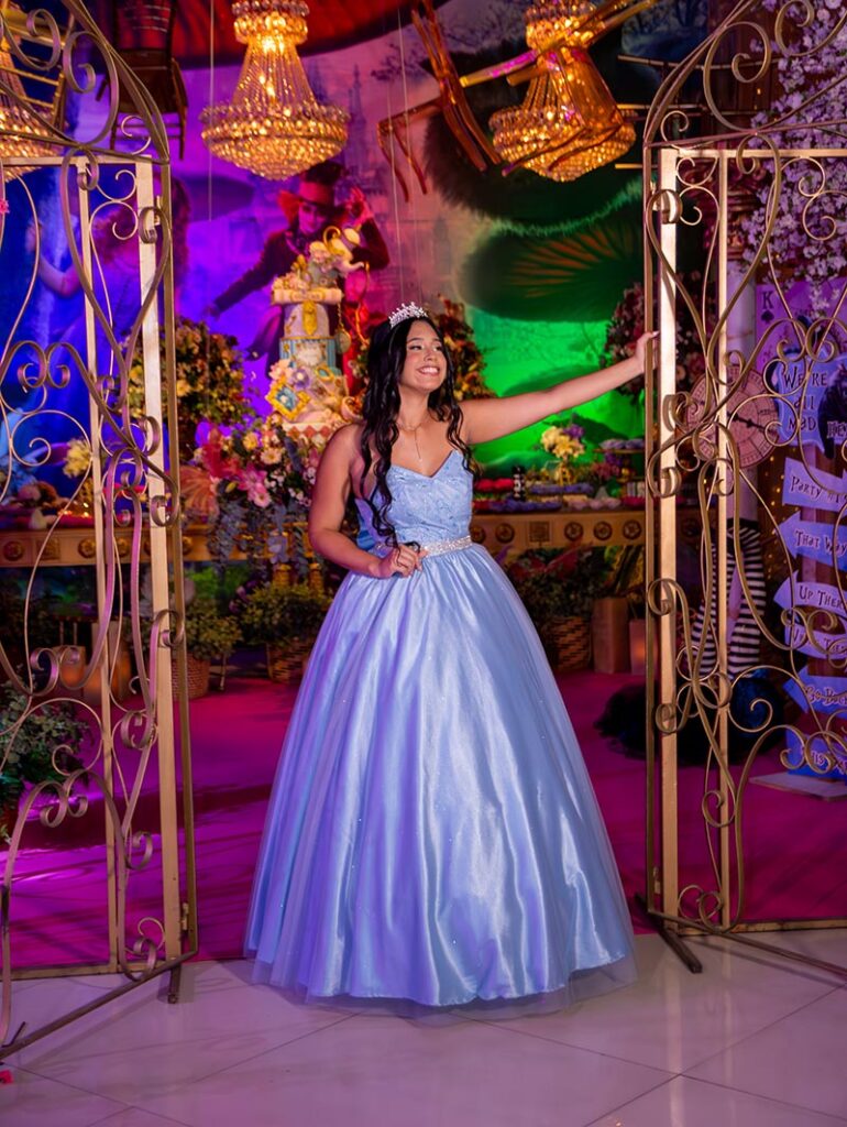 Debutante em vestido azul entre os portais dourados do cenário de Alice no País das Maravilhas