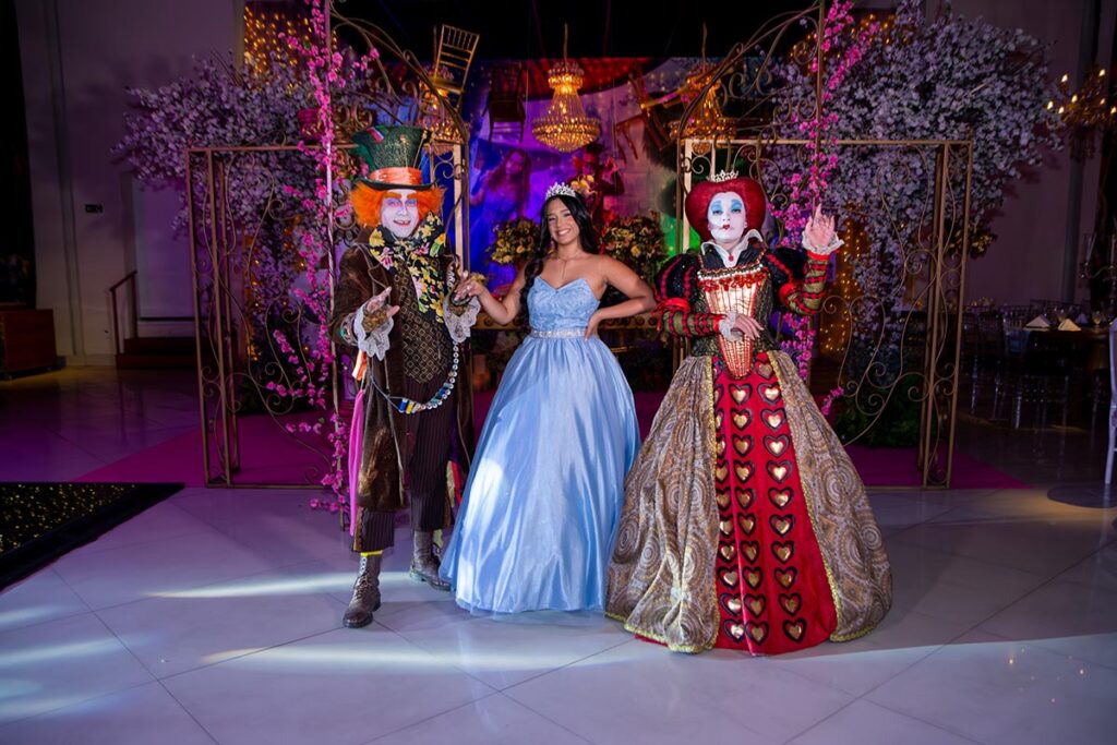 Debutante entre o Chapeleiro Maluco e a Rainha de Copas na pista da festa