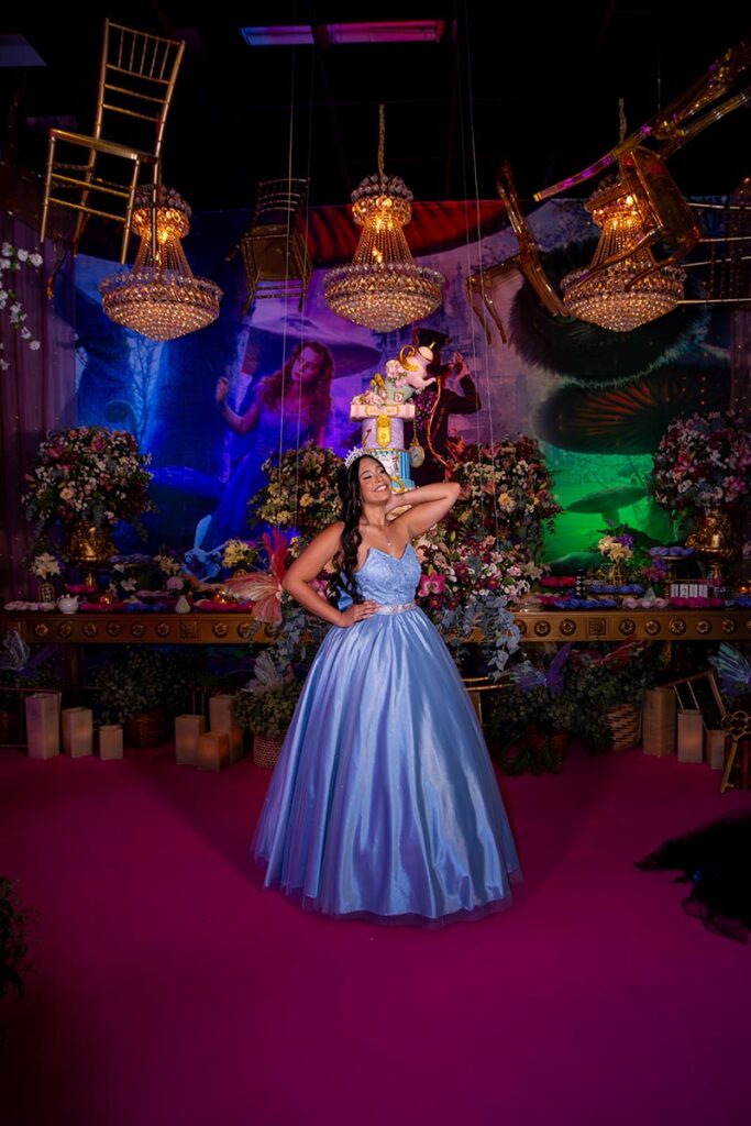 Debutante em vestido azul diante da mesa do bolo iluminada