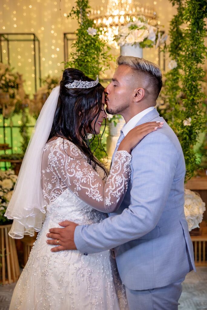Selma e Breno se beijam sob a decoração de flores e folhagens