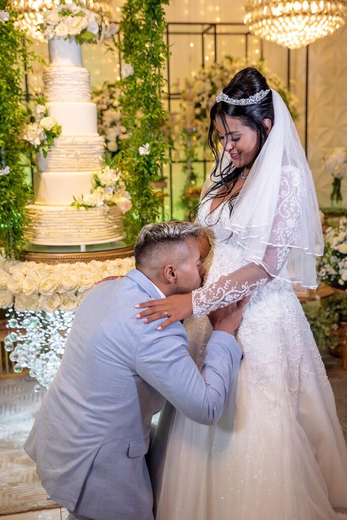 Noivo abraça a noiva diante do bolo de casamento