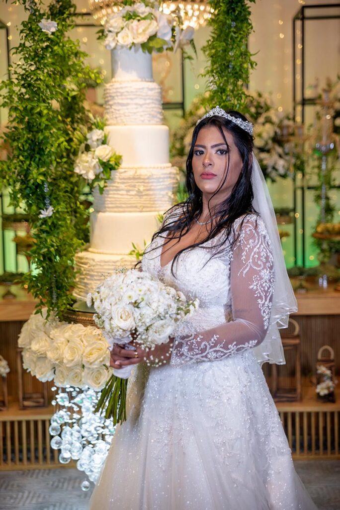 Noiva com o buquê diante do bolo de casamento