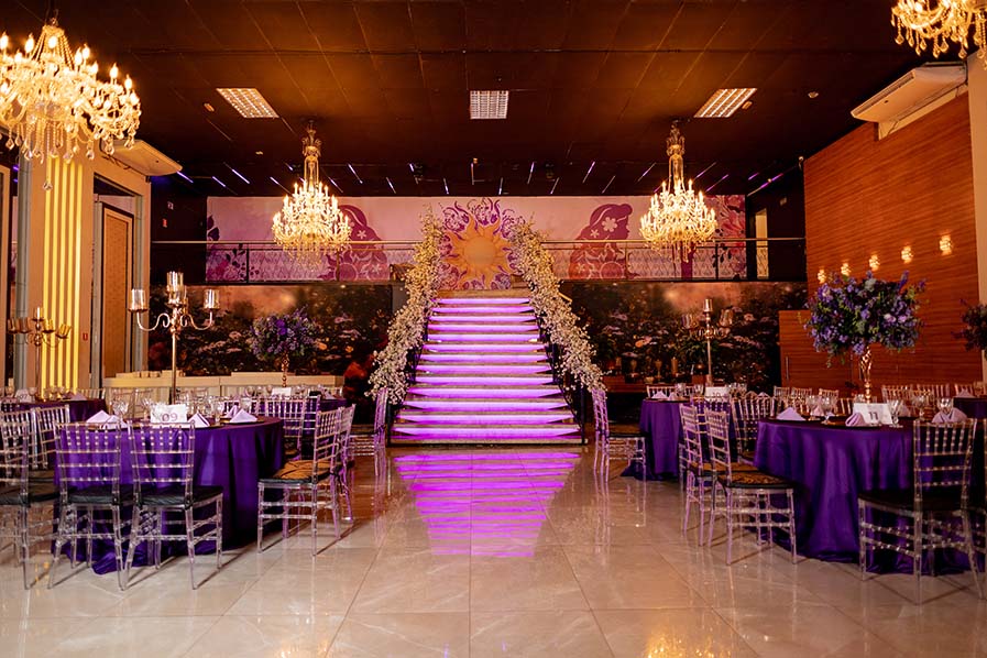 Salão da festa de 15 anos com escadaria central, lustres e mesas em roxo