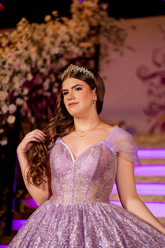 Retrato da debutante em vestido lilás diante da escadaria iluminada