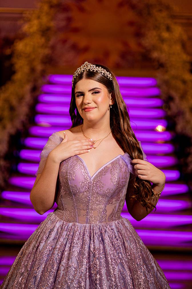Debutante em vestido lilás com a escadaria iluminada ao fundo