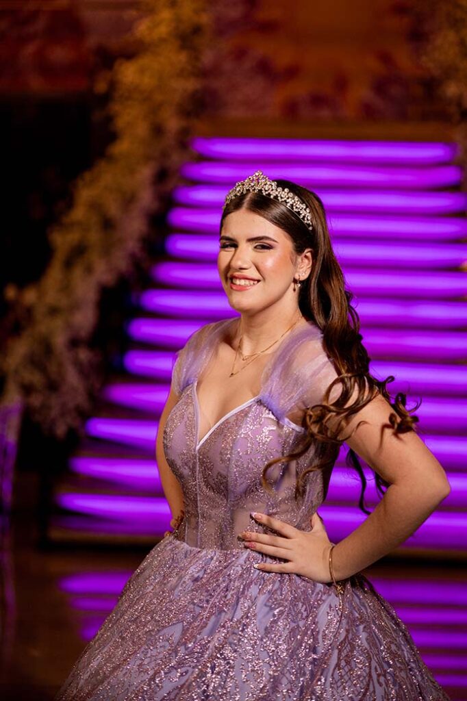 Debutante em vestido lilás ao pé da escadaria iluminada