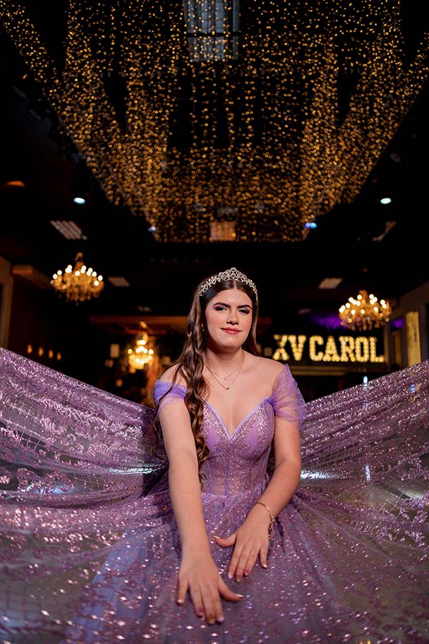 Debutante sentada com o vestido lilás espalhado diante do letreiro
