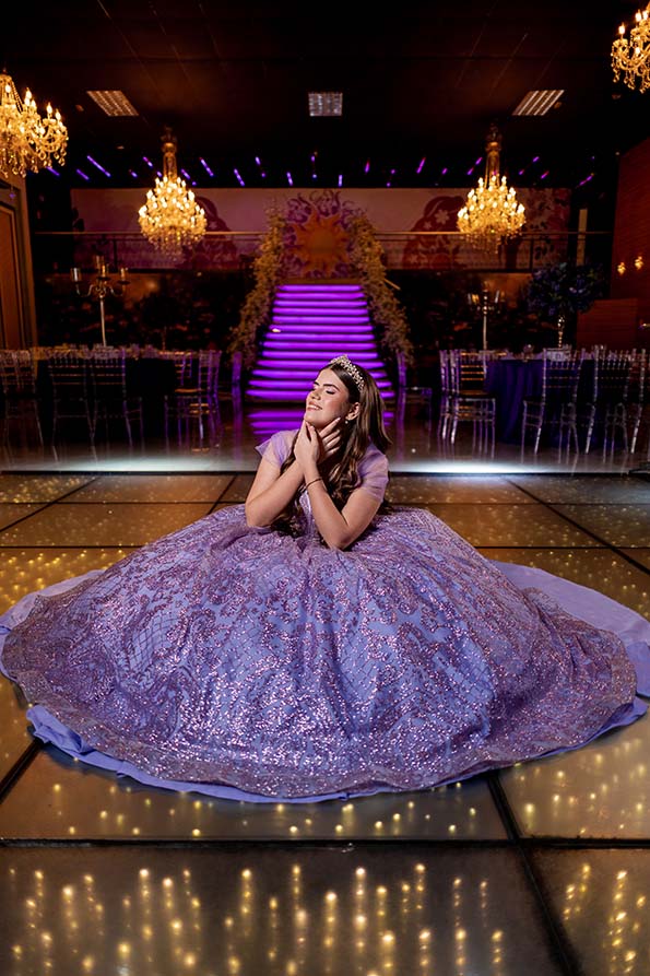 Debutante sentada com o vestido lilás estendido na pista iluminada