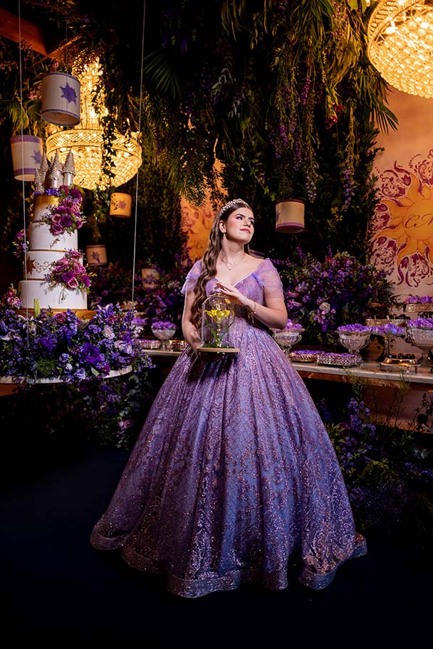 Debutante em vestido lilás diante da mesa do bolo