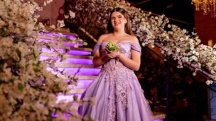 Debutante em vestido lilás na escadaria decorada com flores brancas