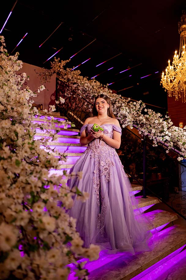 Debutante em vestido lilás na escadaria decorada com flores brancas