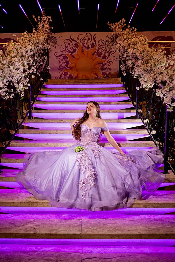 Debutante desce a escadaria iluminada em roxo decorada com flores